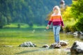 Adorable girl playing by Konigssee lake in Germany on warm summer day. Cute child having fun feeding ducks and throwing stones int Royalty Free Stock Photo