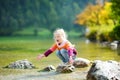 Adorable girl playing by Konigssee lake in Germany on warm summer day. Cute child having fun feeding ducks and throwing stones int Royalty Free Stock Photo