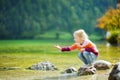 Adorable girl playing by Konigssee lake in Germany on warm summer day. Cute child having fun feeding ducks and throwing stones int Royalty Free Stock Photo