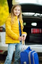 Adorable girl with a suitcase ready to go on vacations with her parents. Child looking forward for a road trip or travel. Autumn b Royalty Free Stock Photo