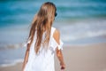 Back view of adorable little girl with long hair in white dress walking on tropical beach vacation Royalty Free Stock Photo