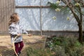 Adorable girl watering spring flowers with a garden hose on a sunny day.