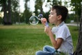 Adorable handsome preadolescent child boy blowing starting soap bubbles on the park, resting during his school recreation Royalty Free Stock Photo