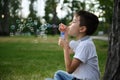 Adorable handsome preadolescent child boy blowing starting soap bubbles on the park, resting during his school recreation Royalty Free Stock Photo