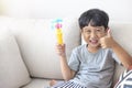 Adorable happy Asian little boy looking at the camera wearing a gray shirt and blue-white striped shorts sitting on a cream sofa Royalty Free Stock Photo