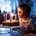 Adorable happy blond little kid boy celebrating his birthday. Child blowing candles on homemade baked cake, indoor Royalty Free Stock Photo