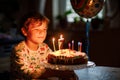 Adorable happy blond little kid boy celebrating his birthday. Child blowing seven candles on homemade baked cake, indoor Royalty Free Stock Photo