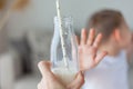 Adorable happy blonde boy in light clothes refuses to drink milk at home. Eco products. Healthy food and drinks Royalty Free Stock Photo