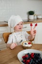 Adorable happy boy in chefs hat and apron puts raspberries on fingers Royalty Free Stock Photo