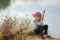 Adorable happy child girl plays with stick on river side in sunny day