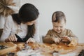 Adorable happy daughter and mother making together christmas cookies on messy table. Cute toddler girl helper with mom cutting Royalty Free Stock Photo