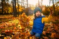 Adorable happy joyful baby girl in bright warm colorful clothes, catching fallen leaves, playing in maple park at sunset. Royalty Free Stock Photo