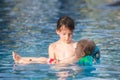 Adorable happy little child, toddler boy, having fun relaxing and playing with his older brother in a pool on sunny day during Royalty Free Stock Photo