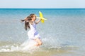 Adorable happy little girl wearing a white dress running through the sea water and playing with the yellow to Royalty Free Stock Photo