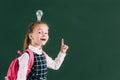 adorable happy schoolchild with backpack and light bulb on head pointing up with finger and smiling
