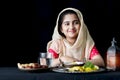 Adorable happy smiling Muslim girl with beautiful eyes wearing hijab and traditional costume sitting at kitchen table, portrait of Royalty Free Stock Photo