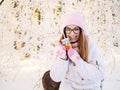 Adorable happy young blonde woman in pink knitted hat scarf having fun drinking hot tea from mug snowy winter park forest in natur Royalty Free Stock Photo