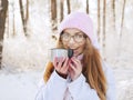 Adorable happy young blonde woman in pink knitted hat scarf having fun drinking hot tea from thermos cup snowy winter park forest Royalty Free Stock Photo