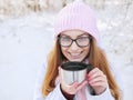 Adorable happy young blonde woman in pink knitted hat scarf having fun drinking hot tea from thermos cup snowy winter park forest Royalty Free Stock Photo
