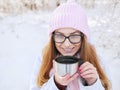 Adorable happy young blonde woman in pink knitted hat scarf having fun drinking hot tea from thermos cup snowy winter park forest Royalty Free Stock Photo