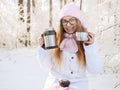 Adorable happy young blonde woman in pink knitted hat scarf having fun drinking hot tea from thermos cup snowy winter park forest Royalty Free Stock Photo