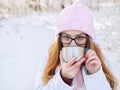 Adorable happy young blonde woman in pink knitted hat scarf having fun drinking hot tea from thermos cup snowy winter park forest Royalty Free Stock Photo