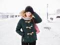 Adorable happy young redhead woman in green parka hat having fun at snowy winter exploring river pier