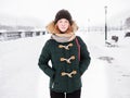 Adorable happy young redhead woman in green parka hat having fun at snowy winter exploring river pier