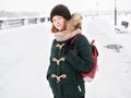 Adorable happy young redhead woman in green parka hat having fun at snowy winter exploring river pier