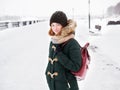 Adorable happy young redhead woman in green parka hat having fun at snowy winter exploring river pier