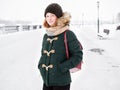 Adorable happy young redhead woman in green parka hat having fun at snowy winter exploring river pier