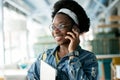 Hipster dark-skinned woman with Afro hairstyle talking on smart phone at cafe. Royalty Free Stock Photo