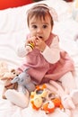 Adorable hispanic baby bitting maraca sitting on bed at bedroom