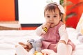 Adorable hispanic baby bitting maraca sitting on bed at bedroom