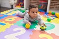 Adorable hispanic baby playing with ball and car lying on floor at kindergarten Royalty Free Stock Photo