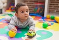 Adorable hispanic baby playing with ball and car lying on floor at kindergarten Royalty Free Stock Photo