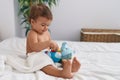 Adorable hispanic baby sitting on bed playing with elephant doll at bedroom Royalty Free Stock Photo