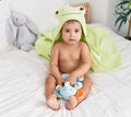 Adorable hispanic baby wearing frog towel playing with elephant toy at bedroom Royalty Free Stock Photo