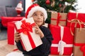 Adorable hispanic boy hearing gift sound sitting on floor by christmas tree at home
