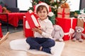 Adorable hispanic boy hearing gift sound sitting on floor by christmas tree at home