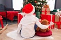 Adorable hispanic boy hugging teddy bear sitting on floor by christmas tree at home Royalty Free Stock Photo