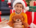 Adorable hispanic boy hugging teddy bear sitting on floor by christmas tree at home Royalty Free Stock Photo