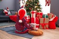 Adorable hispanic boy hugging teddy bear sitting on floor by christmas tree at home Royalty Free Stock Photo