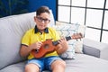 Adorable hispanic boy playing ukulele sitting on sofa at home Royalty Free Stock Photo