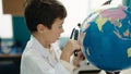 Adorable hispanic boy student looking earth using magnifying glass at laboratory classroom