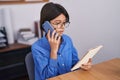 Adorable hispanic girl business worker talking on smartphone reading notebook at office Royalty Free Stock Photo