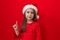 Adorable hispanic girl in christmas hat, finger pointing up