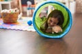 Adorable hispanic girl crawling inside tunnel toy at kindergarten