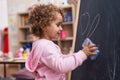 Adorable hispanic girl erasing blackboard at kindergarten