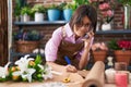 Adorable hispanic girl florist talking on smartphone writing on notebook at flower shop Royalty Free Stock Photo